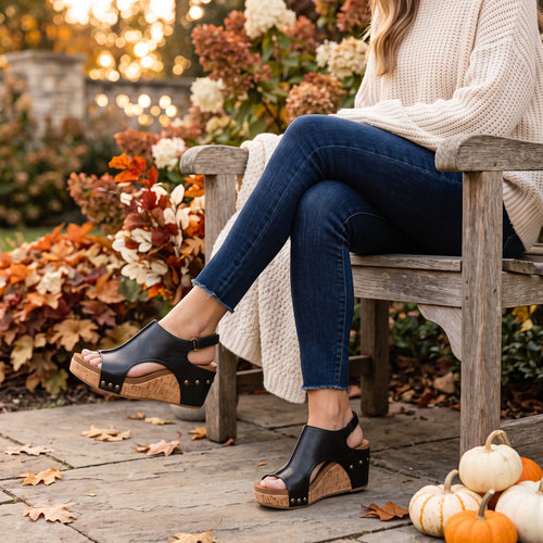 Heel Yeah Boutique Carly wedge sandals in black leather with cork platform, worn by a woman in a fall garden setting.