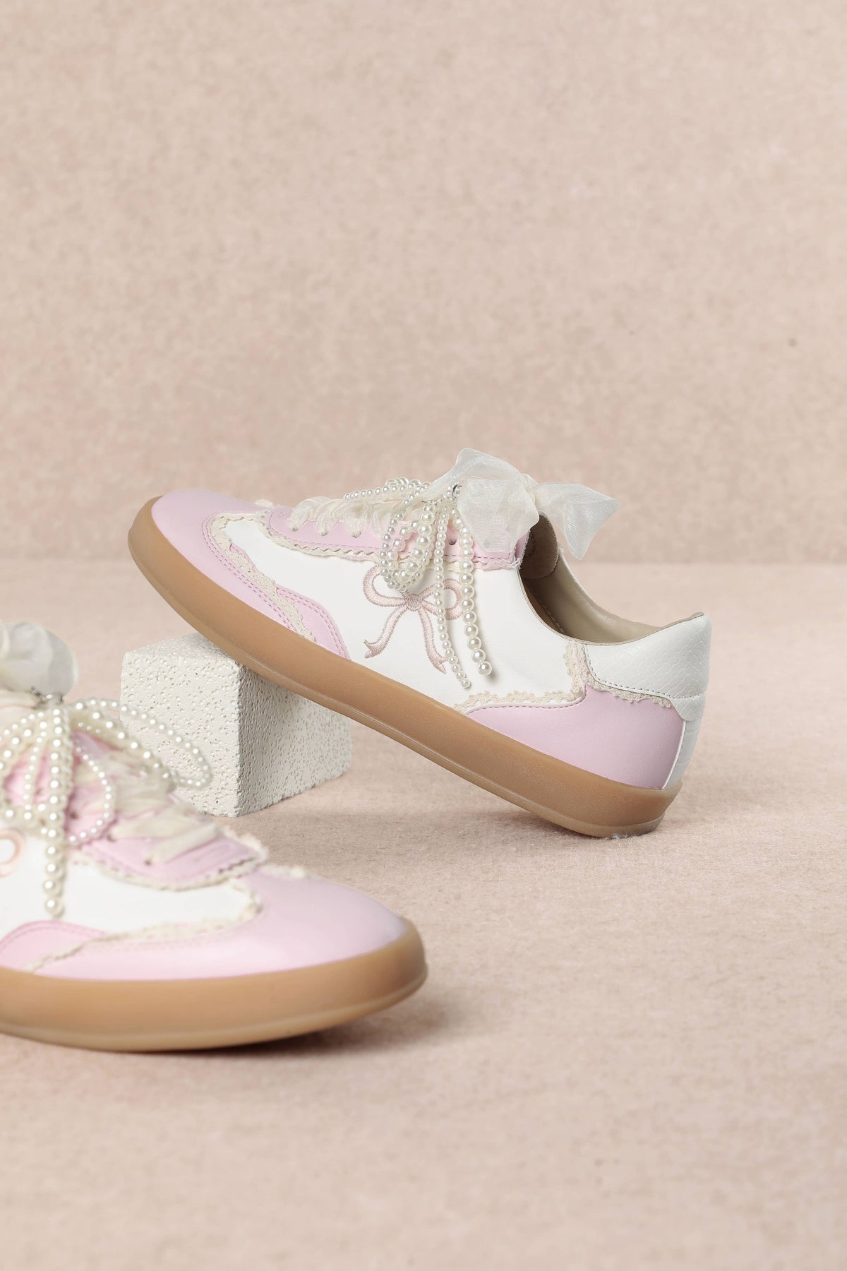Heel Yeah Boutique Julie cream and pink sneakers with sheer ribbon laces, pearl accents, and embroidered bow motifs.