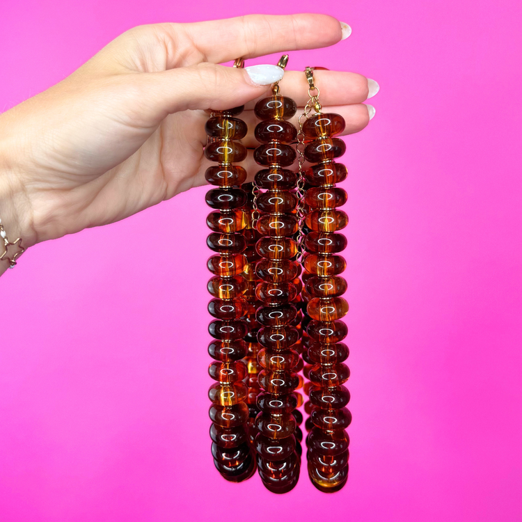 Heel Yeah Boutique tortoise beaded necklace with glossy brown resin beads held in a hand against a bright pink background