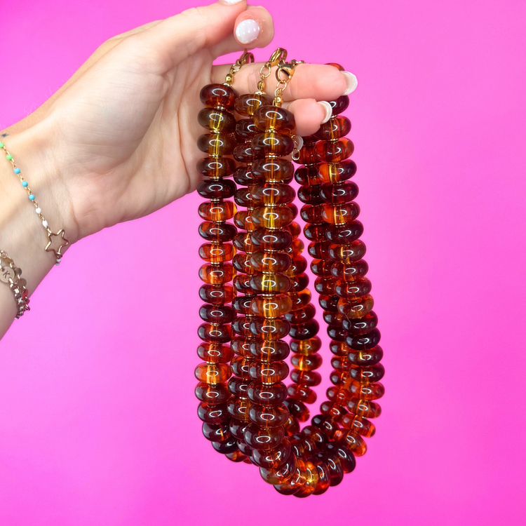 Heel Yeah Boutique tortoise beaded necklace with glossy brown resin beads held against a bright pink background